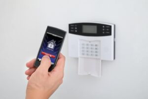 Panel sterujący alarmem domowym i smartfon, który umożliwia zdalne zarządzanie systemem zabezpieczeń.